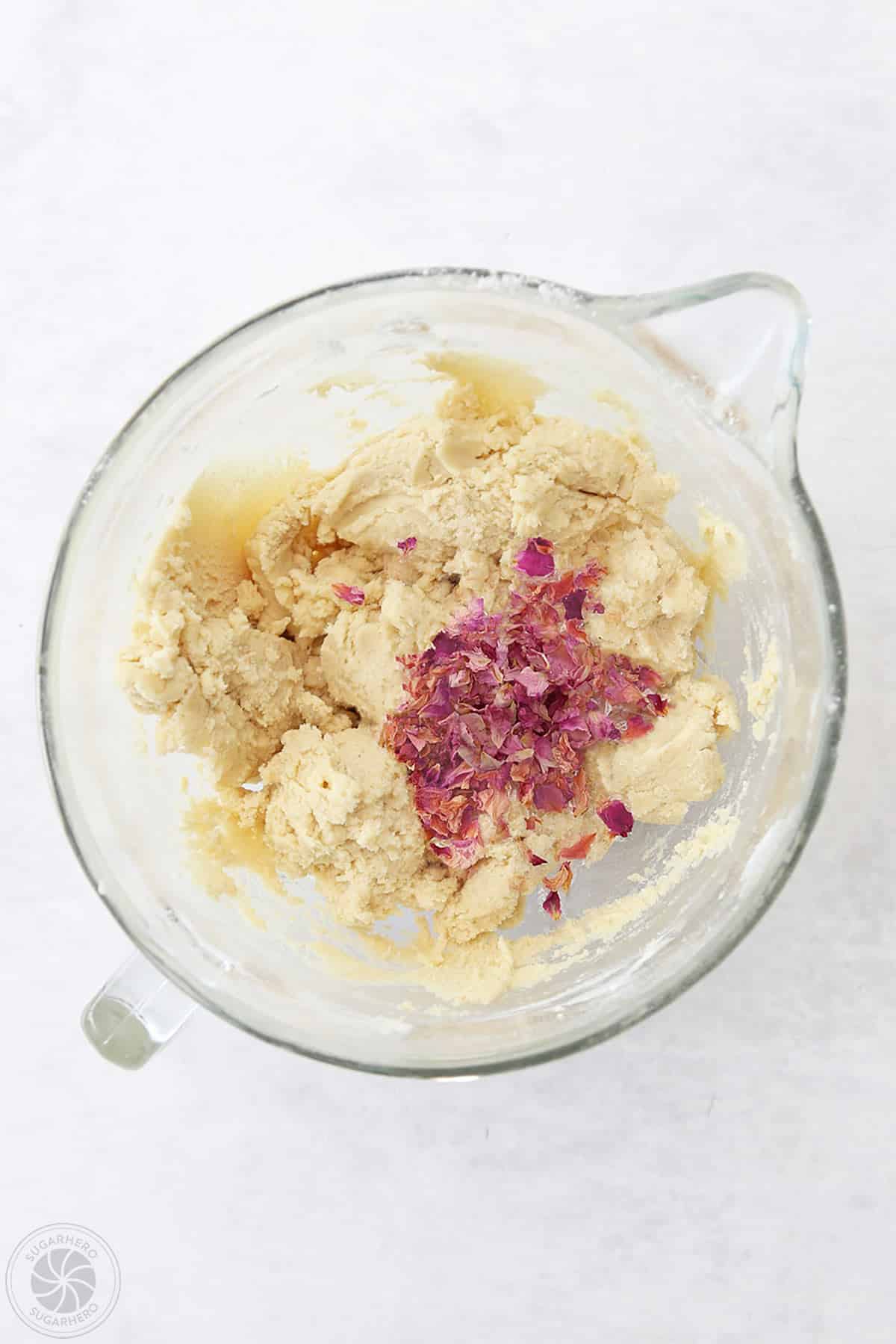 A bowl of sugar cookie dough with dried edible rose petals.