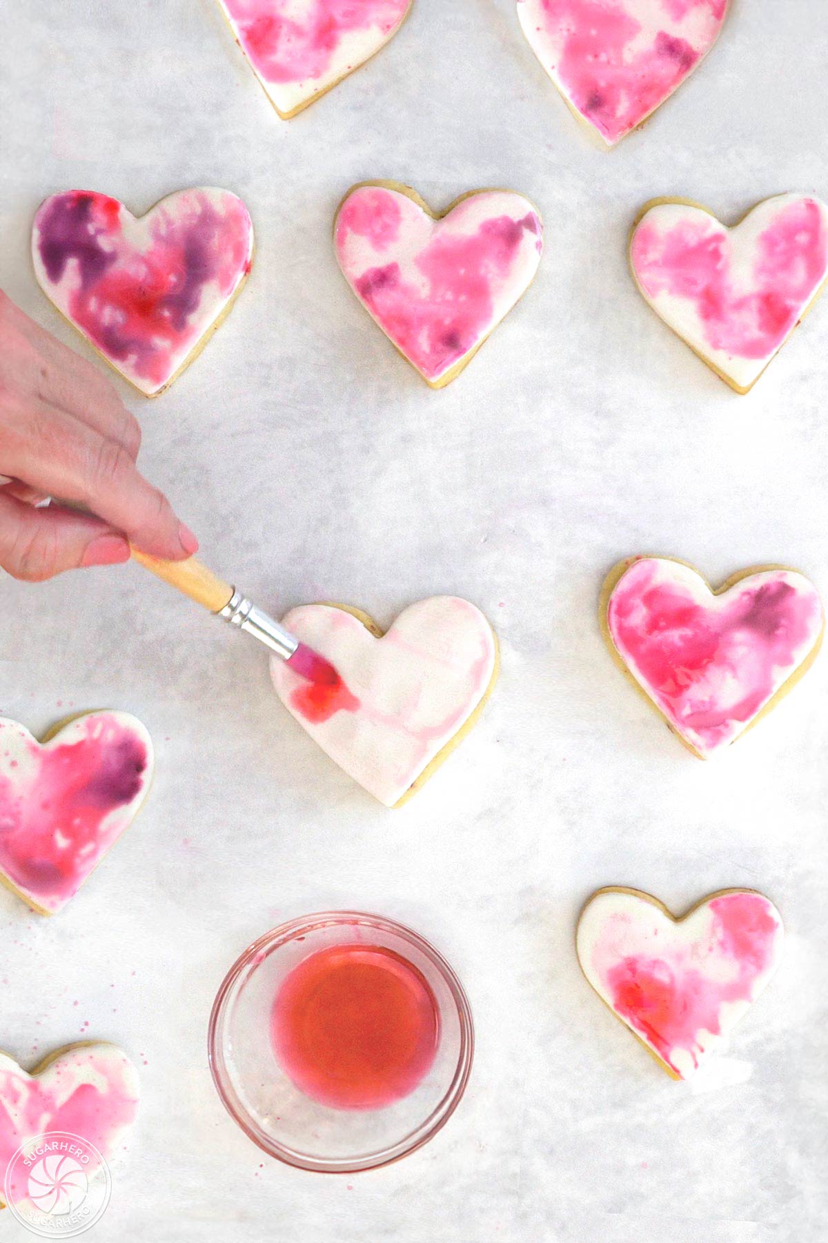 Hand painting watercolor design on a sugar cookie next to other painted cookies.