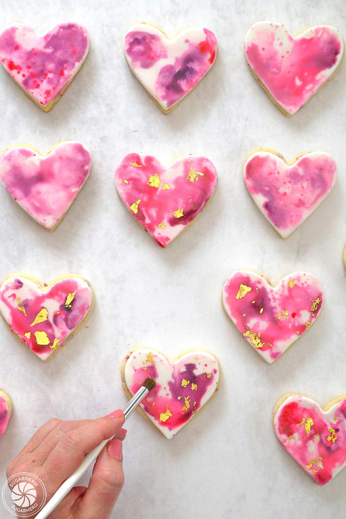 Hand using a paint brush to secure gold leaf to watercolored sugar cookies.