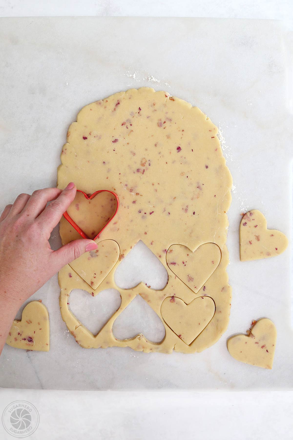 Hand cutting heart shaped cookies from rose sugar cookie dough.