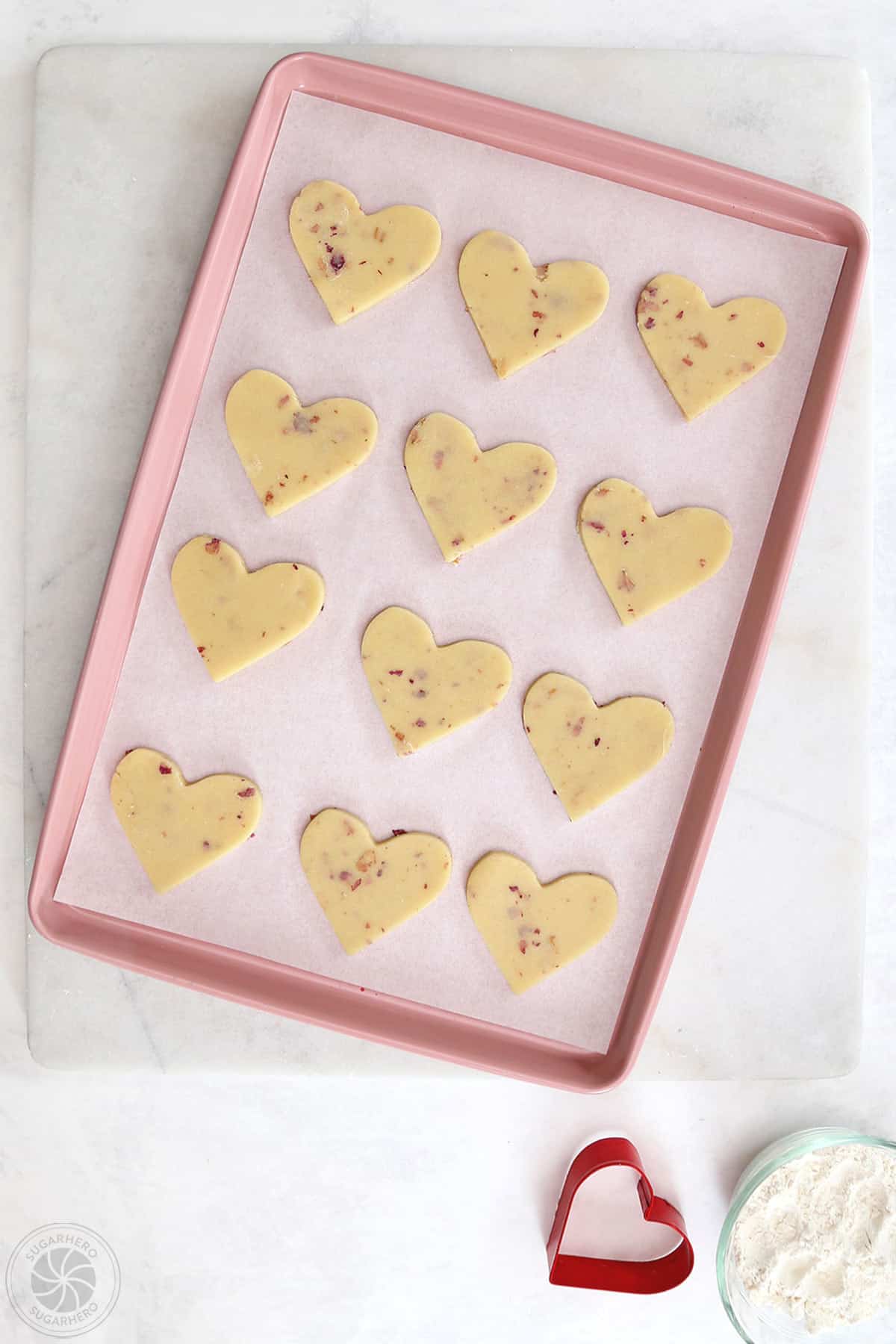 Heart-shaped rose sugar cookies on a parchment lined baking sheet ready to be baked.