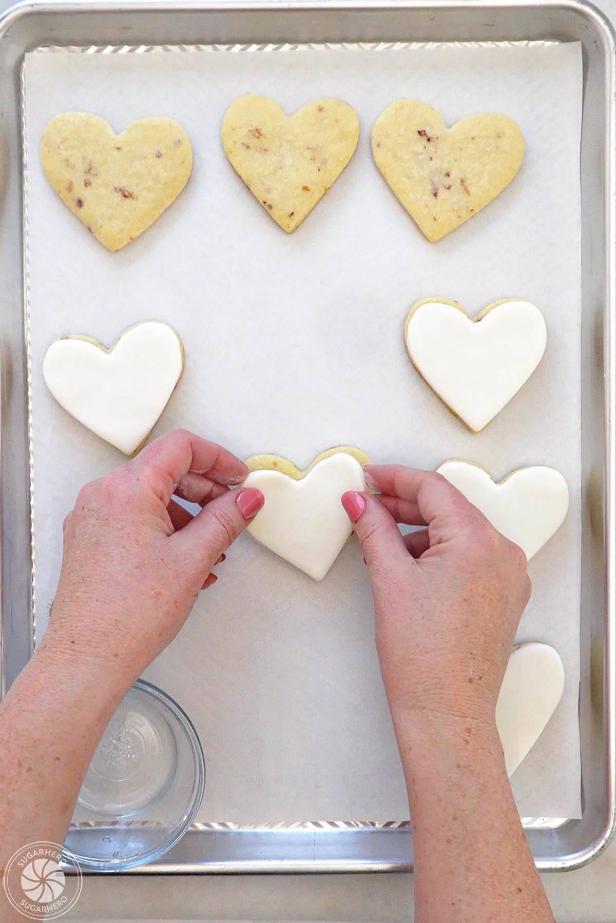 Hand placing fondant hearts on top of baked heart-shaped rose sugar cookies.