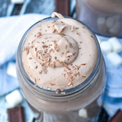 Top view of Whipped Hot Chocolate on a blue background and surrounded by chocolate and marshmallows.