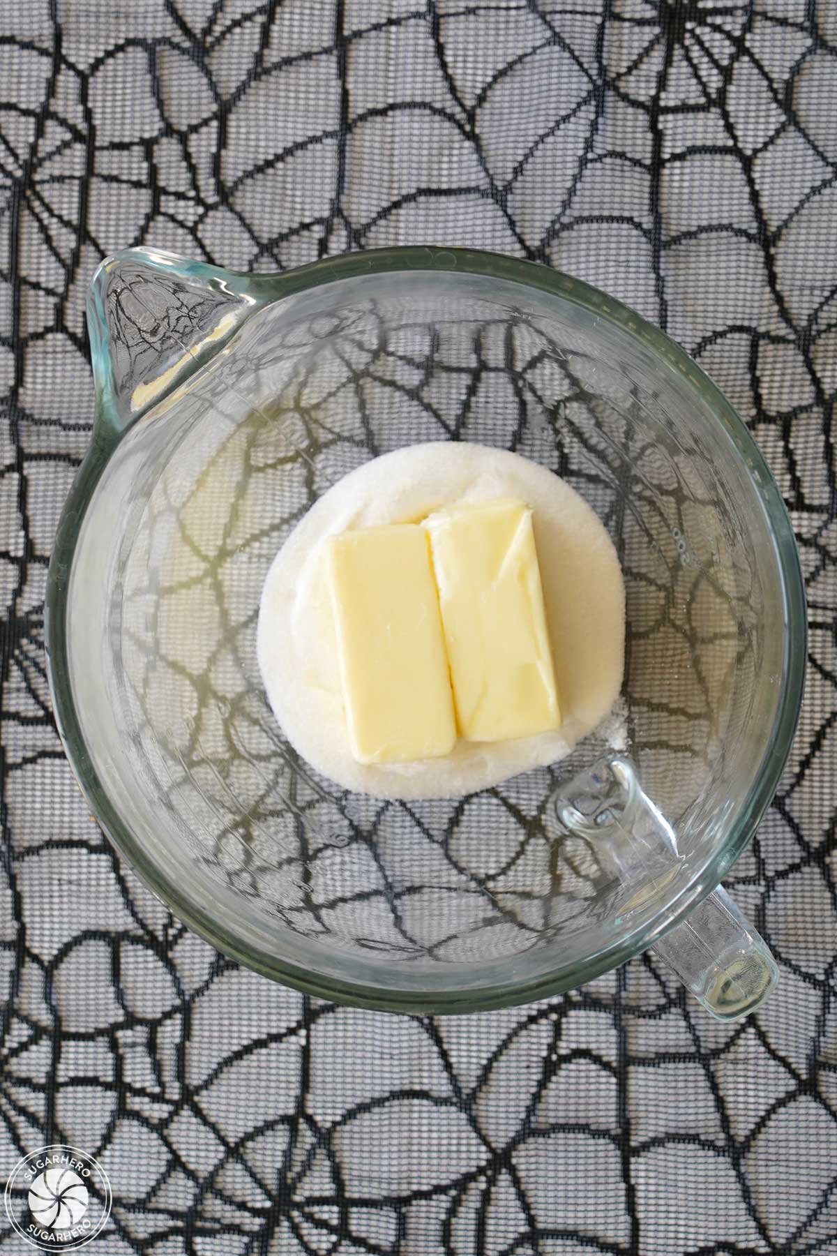 Overhead shot of granulated sugar and 2 sticks of butter in a glass mixing bowl.
