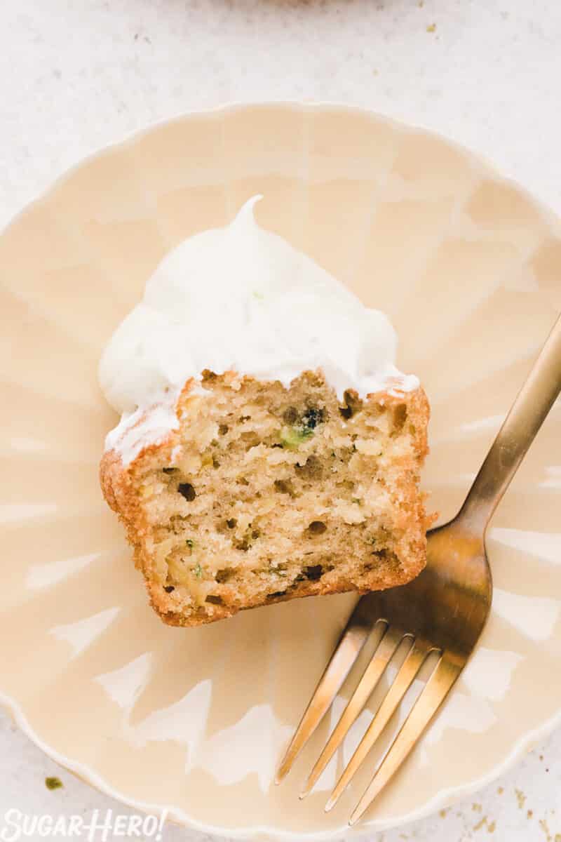 Zucchini cupcake cut in half, on a pink plate with a gold fork next to it.